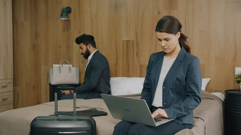 A woman in a blazer using a laptop on a hotel bed
