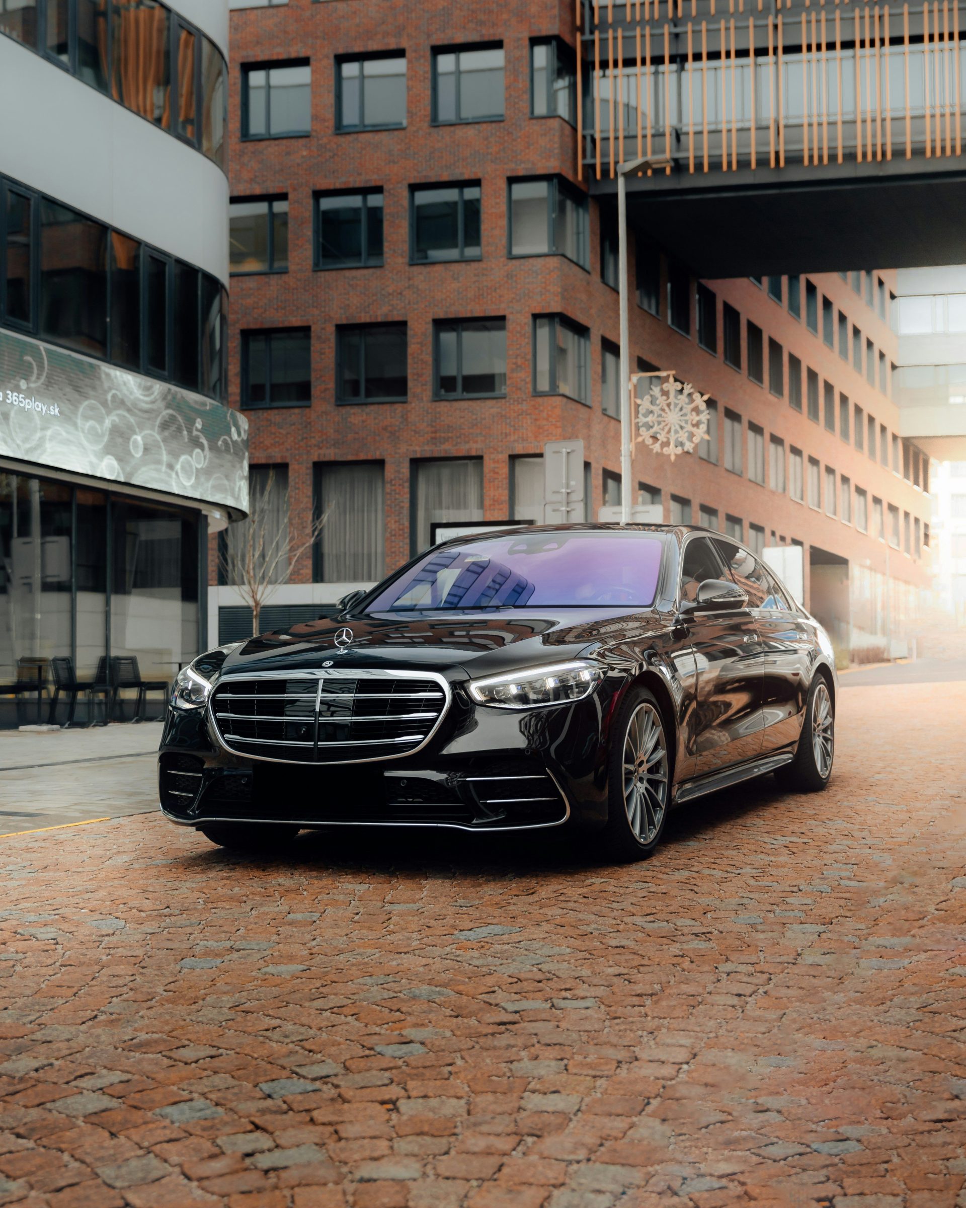 A black Mercedes-Benz sedan parked on a cobblestone street in front of brick buildings
