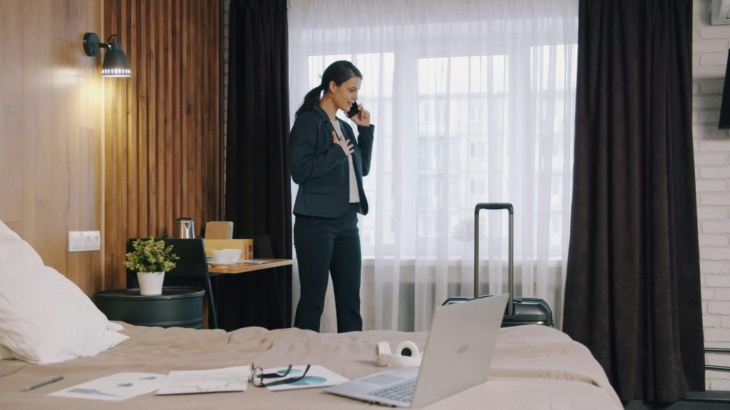 A woman in a dark suit talking on a phone in a hotel room